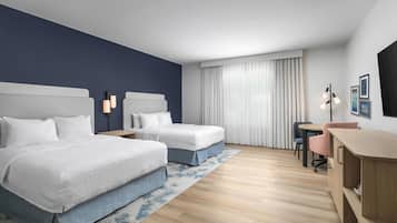 A hotel room with two beds, a desk, a chair, a lamp, and a window with curtains.