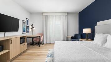 A hotel room with a bed, a desk, a chair, a TV, and a window with curtains.