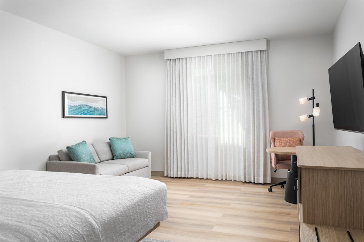 A modern hotel room with a bed, a sofa, a desk, and a TV.