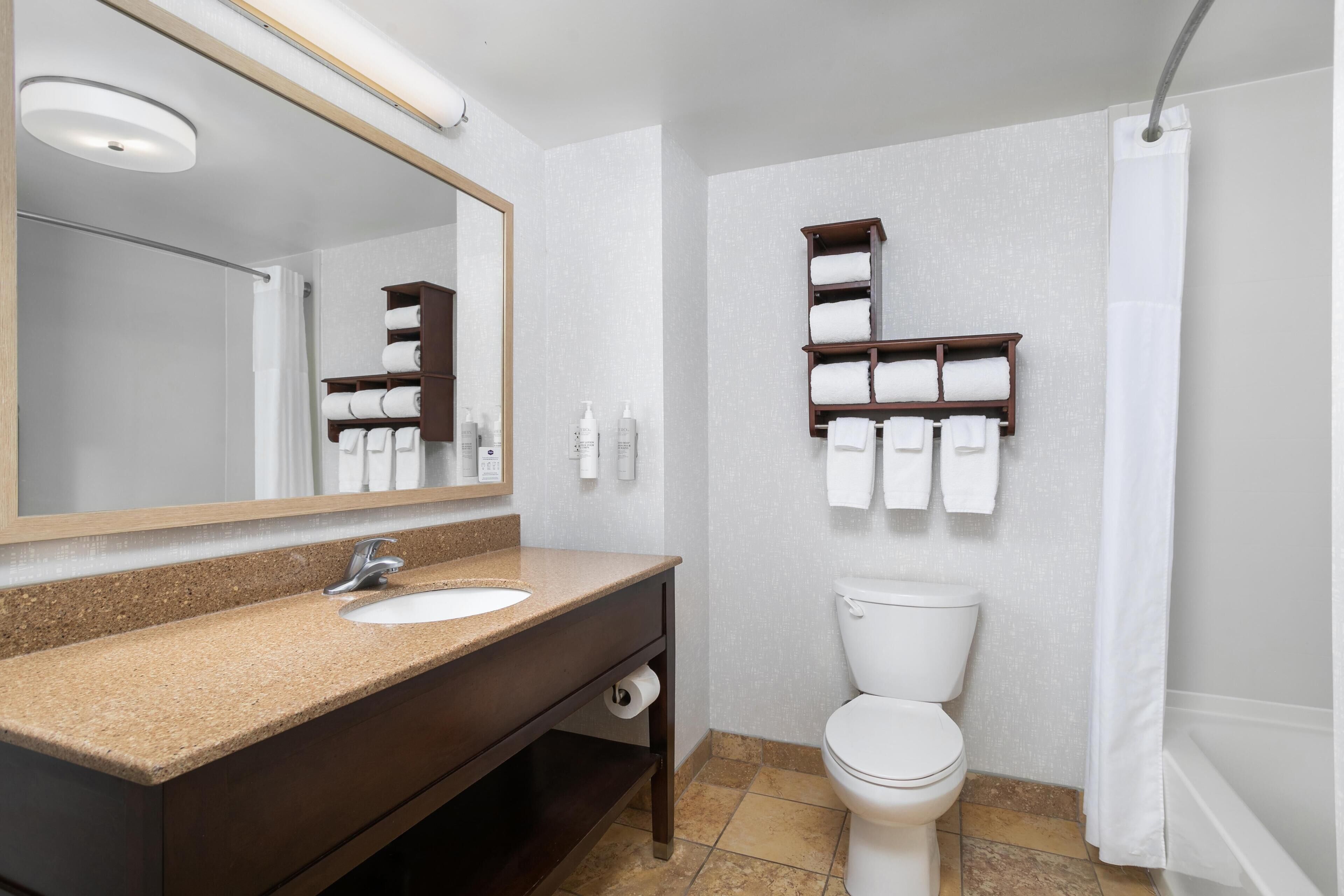 Un bagno con lavandino, specchio, water, porta asciugamani e tenda per la doccia.