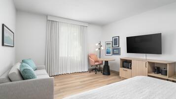 Et moderne hotelværelse med seng, sofa, skrivebord, stol, fjernsyn og mikroovn.