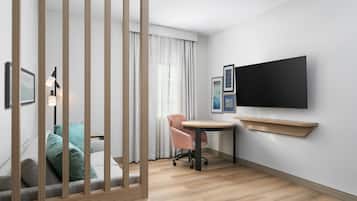 Una habitación de hotel moderna con piso de madera, un escritorio con silla, televisor montado en la pared y una ventana con cortinas.