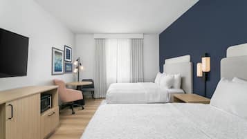 Une chambre d’hôtel avec deux lits, un bureau, une chaise, une télévision et une fenêtre avec des rideaux.