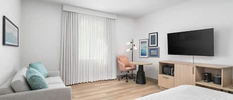Ein modernes Hotelzimmer mit Bett, Sofa, Schreibtisch, Stuhl, Fernseher und einer Mikrowelle.