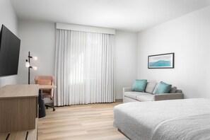 Une chambre d’hôtel moderne équipée d’un lit, d’un bureau, d’une chaise, d’un canapé et d’une grande fenêtre avec des rideaux.