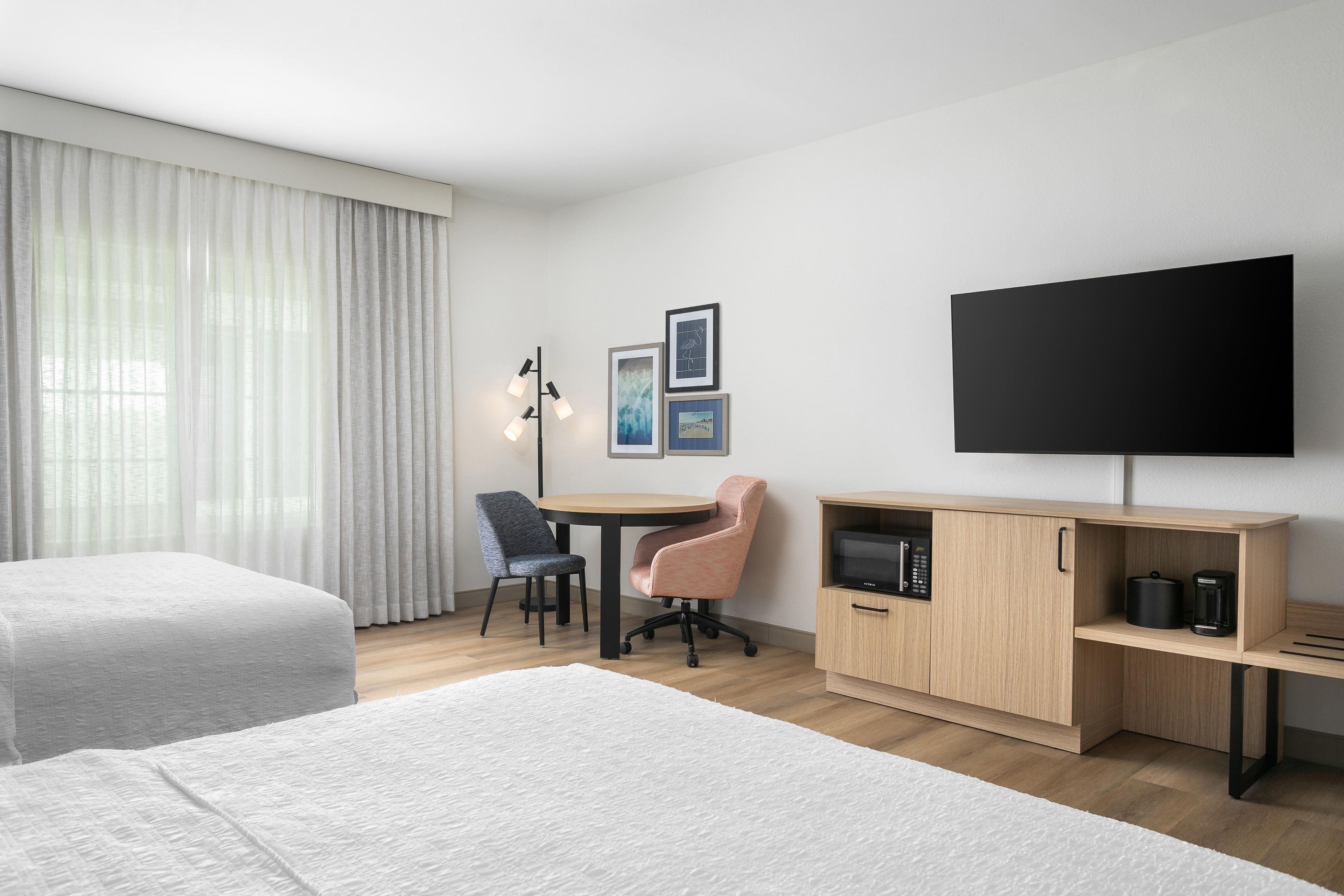 A hotel room with two beds, a desk, a chair, a TV, and a coffee maker.