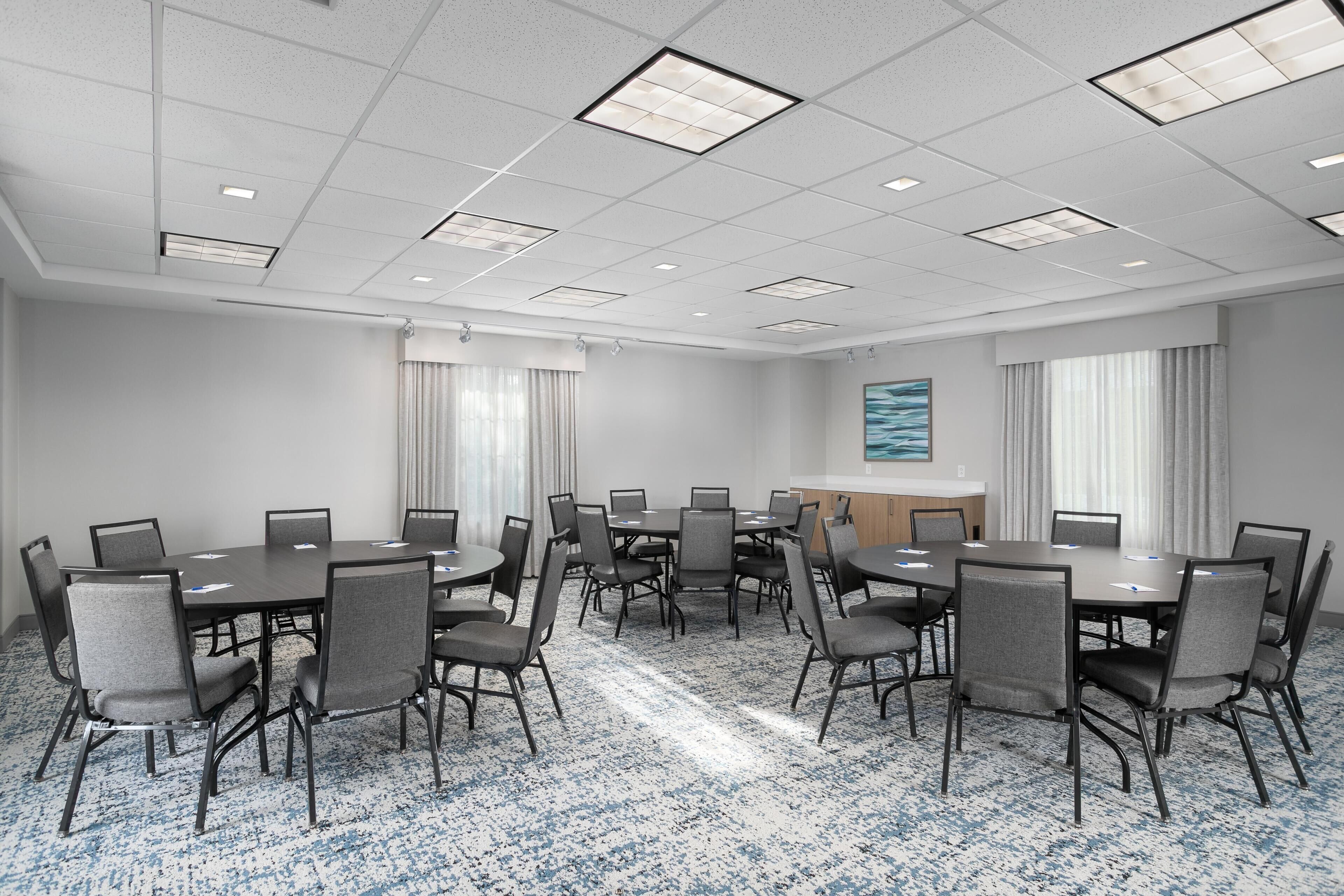 A conference room with a large table, multiple chairs, a carpeted floor, and a painting on the wall.