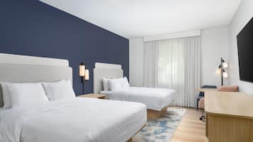 Habitación de hotel con dos camas, un escritorio, una silla y un ventanal con cortinas.