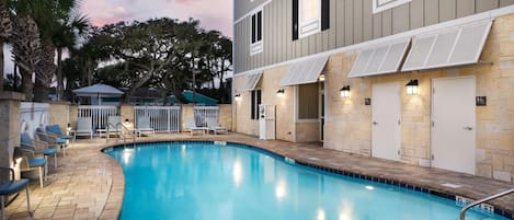 A swimming pool with lounge chairs, a covered seating area, and a building with awnings and doors.