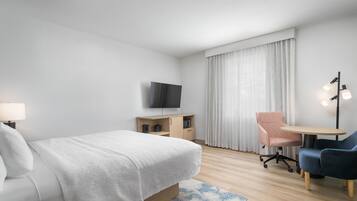 A hotel room with a bed, a desk, a chair, a TV, and a lamp.