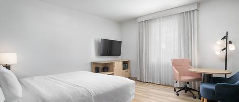 A hotel room with a bed, a desk, a chair, a TV, and a lamp.