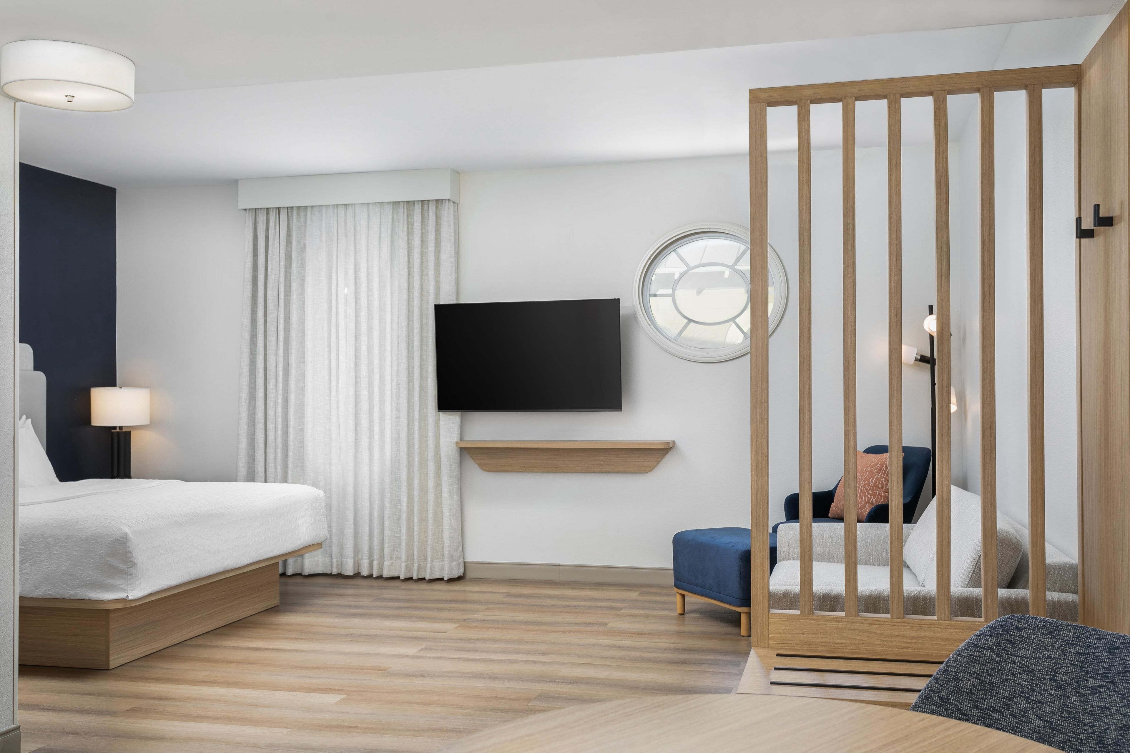A modern hotel room with a bed, a TV, a desk, and a seating area.