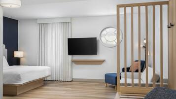 A modern hotel room with a bed, a TV, a desk, and a seating area.