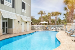A swimming pool with a curved edge, surrounded by lounge chairs and a covered seating area.