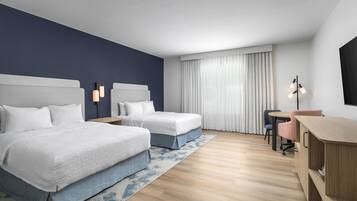 Habitación de hotel con dos camas, un escritorio, una silla y un ventanal con cortinas.