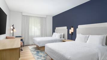 A hotel room with two beds, a desk, a chair, a lamp, and a window with curtains.