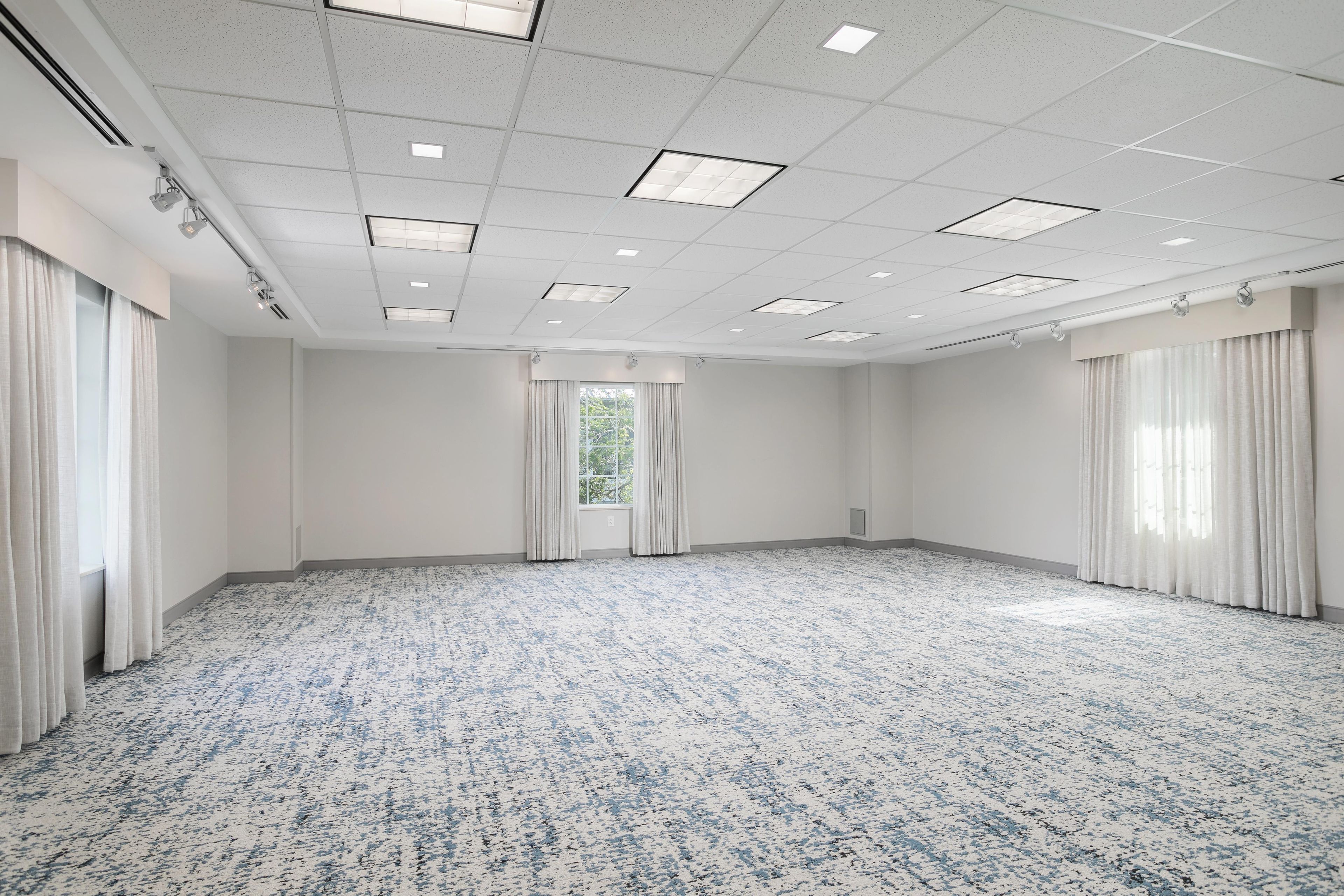 Une grande salle de conférence vide, avec un tapis à motifs, des murs blancs et une grille de luminaires au plafond.
