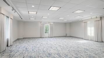 Une grande salle de conférence vide, avec un tapis à motifs, des murs blancs et une grille de luminaires au plafond.