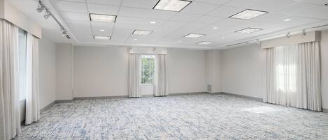 Une grande salle de conférence vide, avec un tapis à motifs, des murs blancs et une grille de luminaires au plafond.