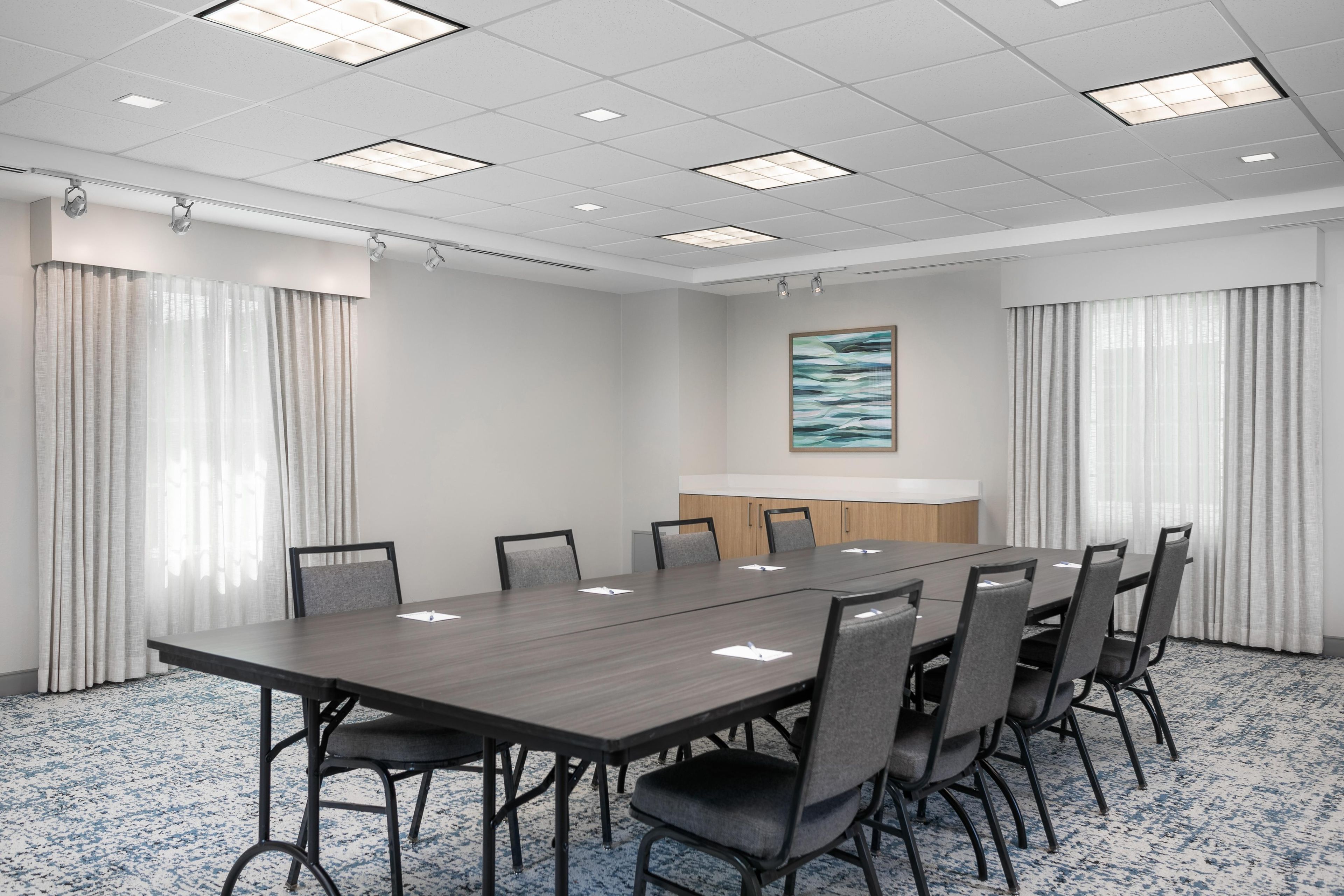 Uma sala de conferência com uma mesa comprida, cadeiras, um quadro branco e um quadro na parede.
