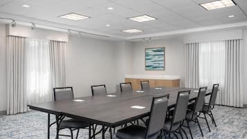 Uma sala de conferência com uma mesa comprida, cadeiras, um quadro branco e um quadro na parede.