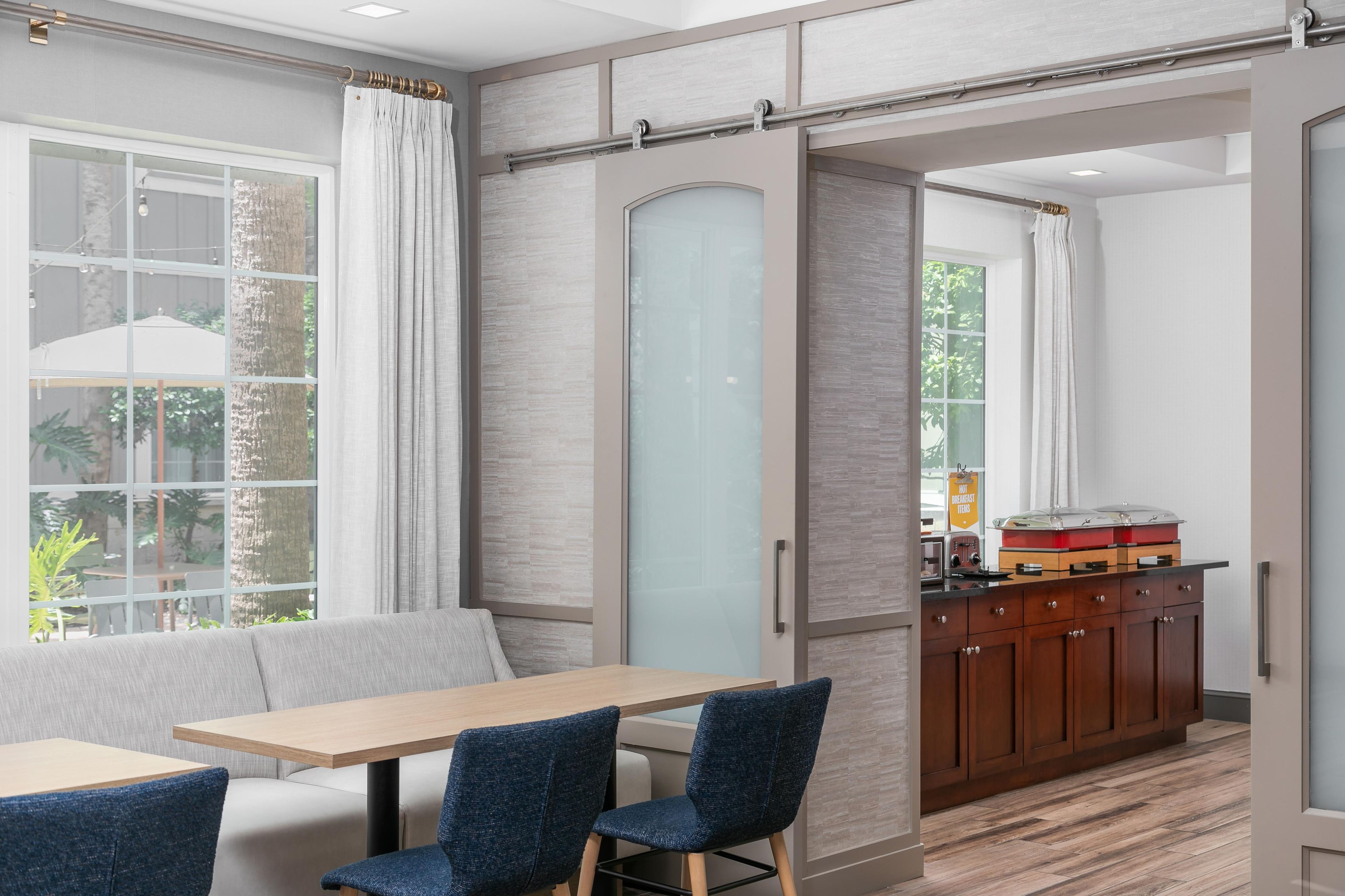 A modern dining area with a wooden table, blue chairs, and a sliding glass door leading to a kitchen with wooden cabinets.