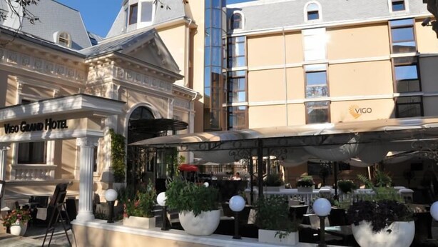 The Vigo Grand Hotel with a covered outdoor seating area and large planters.