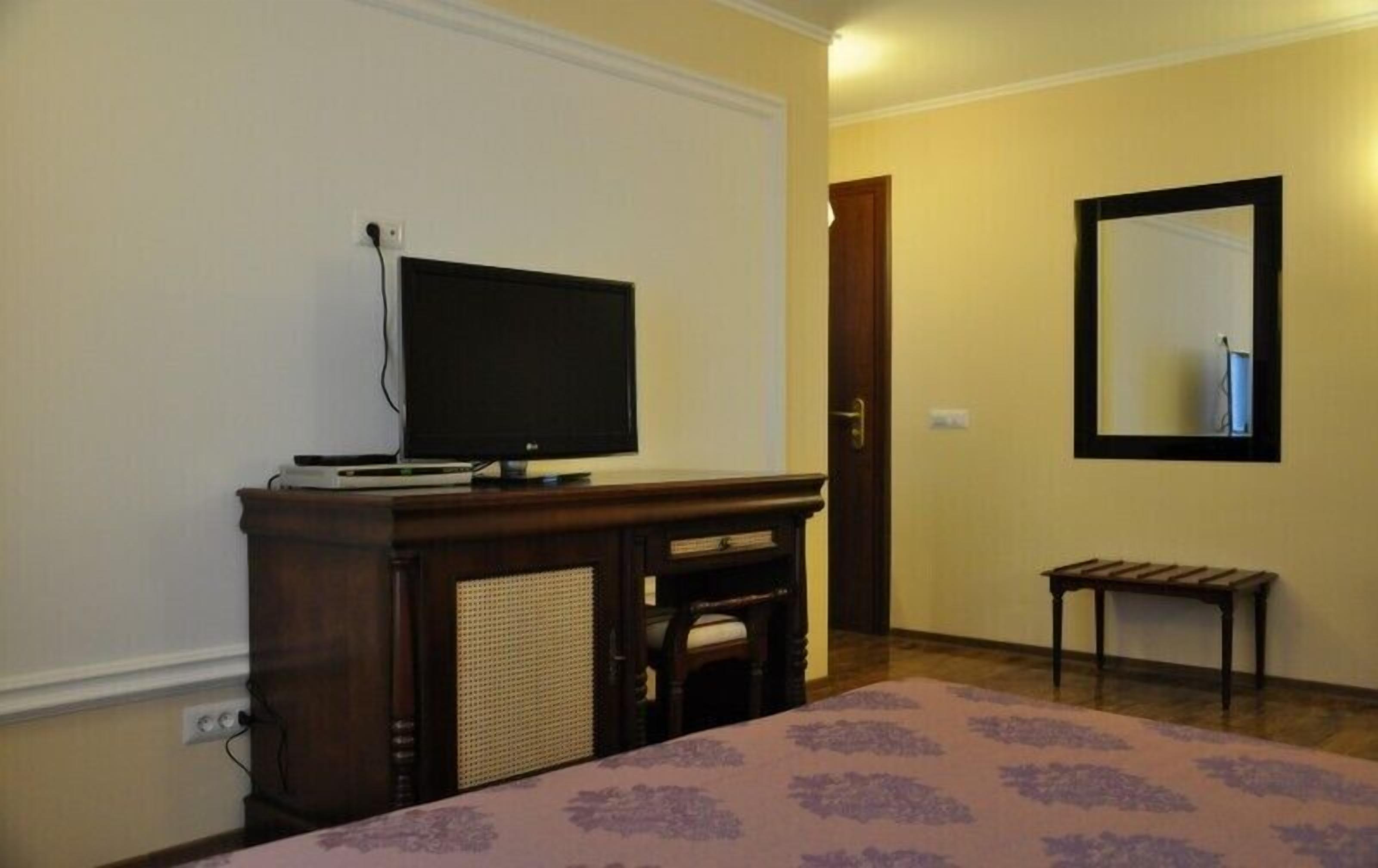 Une chambre d’hôtel avec un lit, un téléviseur posé sur un meuble en bois, une petite table et un miroir au mur.