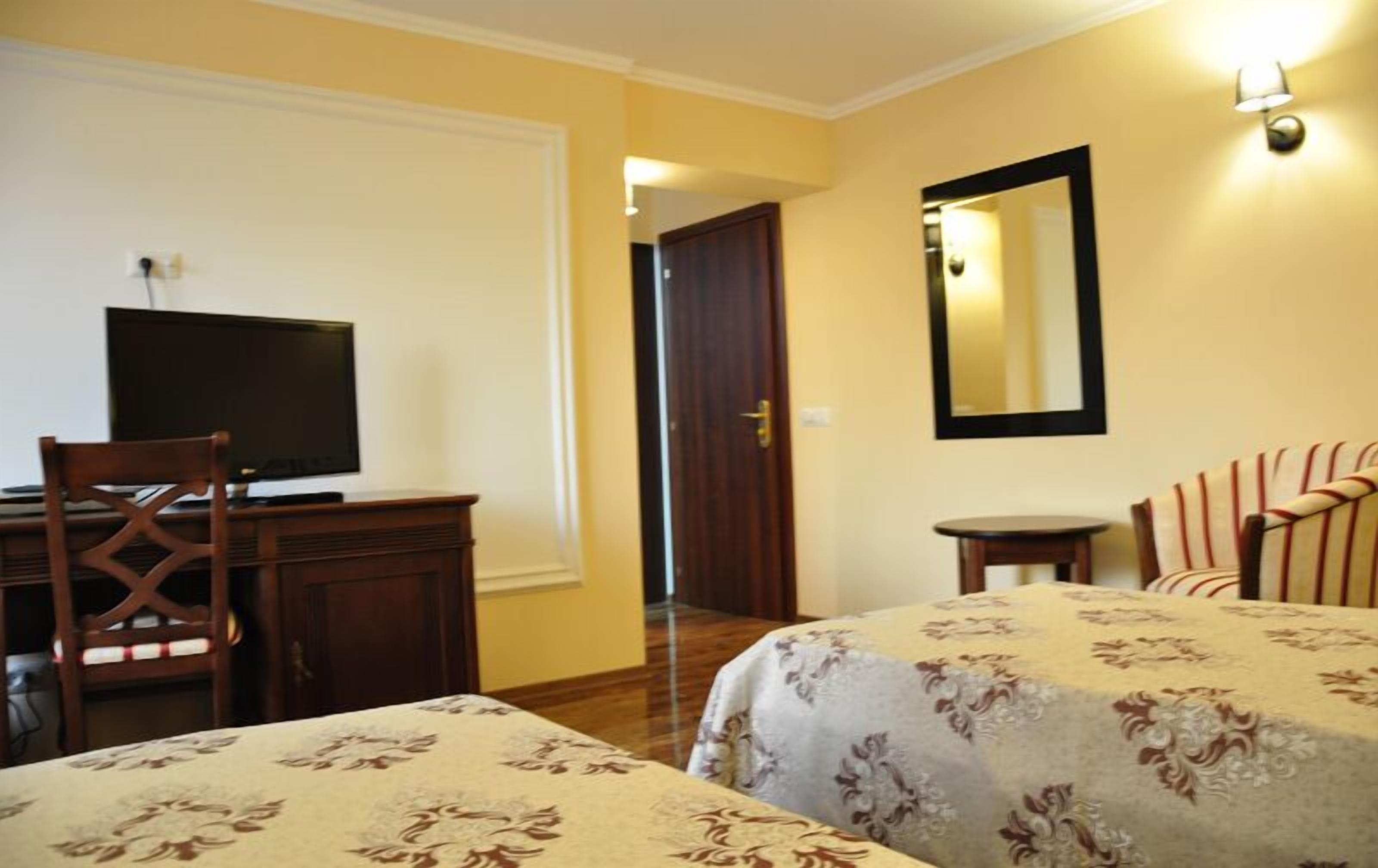 Habitación de hotel con dos camas, un escritorio con televisor, una silla, una mesita y un espejo.