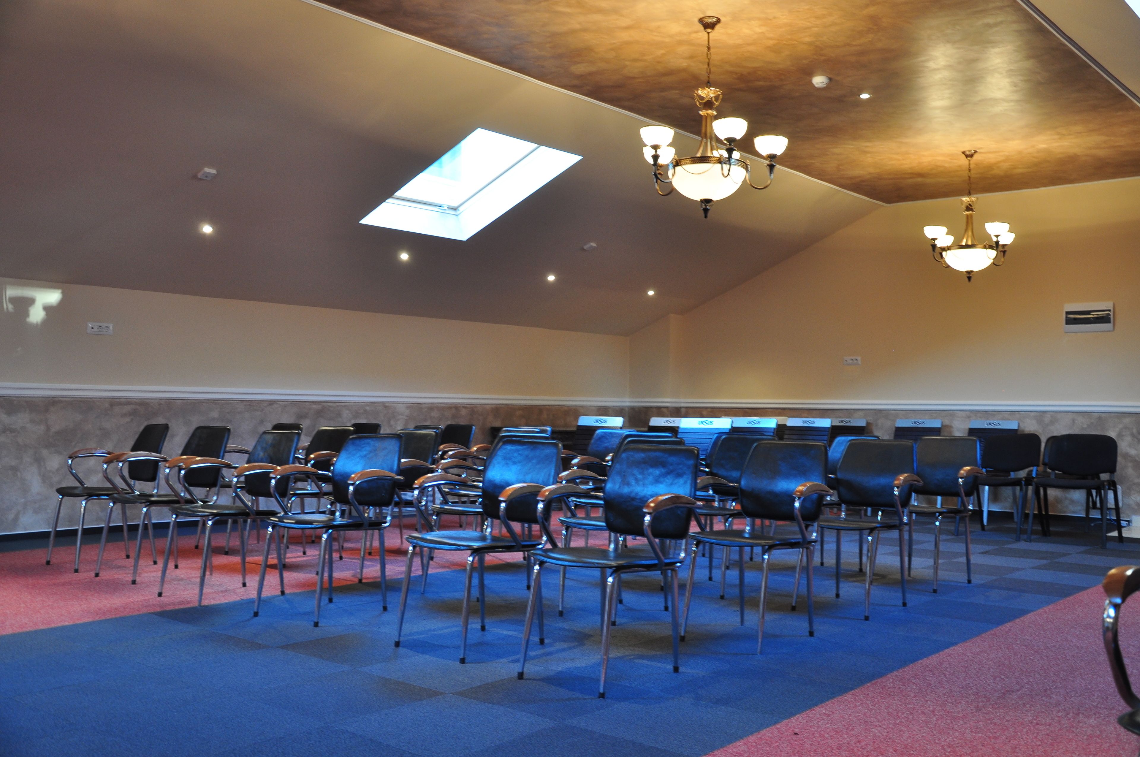 Uma sala de conferências com fileiras de cadeiras, um claraboia e lustres.