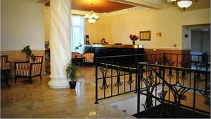 A lobby with a marble floor, a reception desk, striped chairs, and a large column.