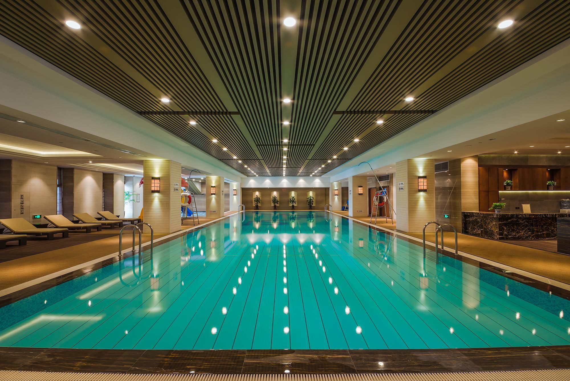 A large indoor swimming pool with multiple lanes, lounge chairs, and a reception area.