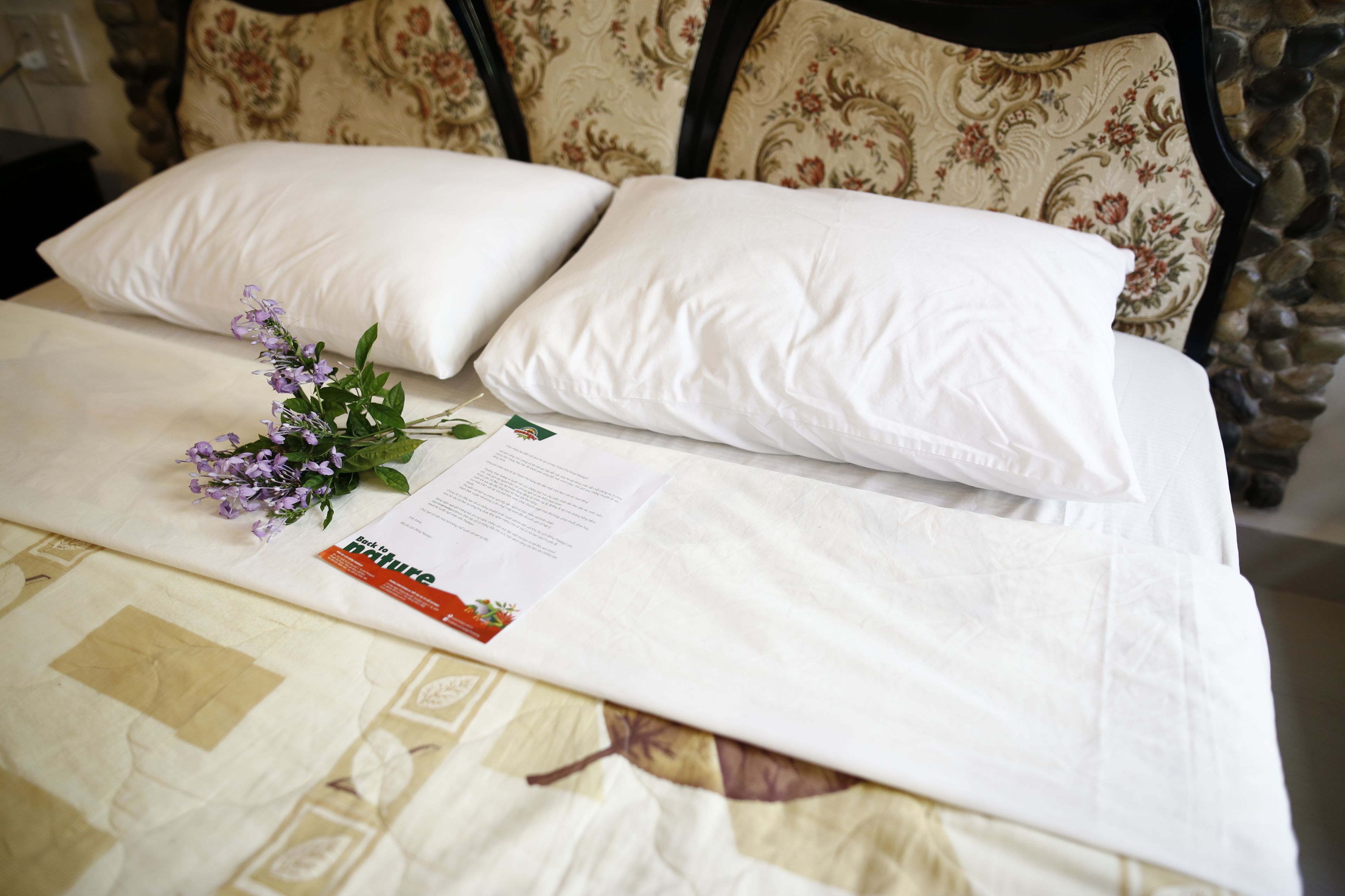 A neatly made bed with white linens, a floral-patterned pillow, and a booklet on the bed.