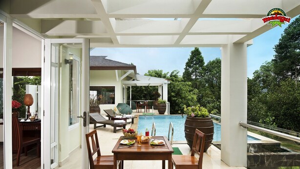 Un área de comedor exterior moderna con piscina, mobiliario de madera y vistas a la piscina y al follaje.