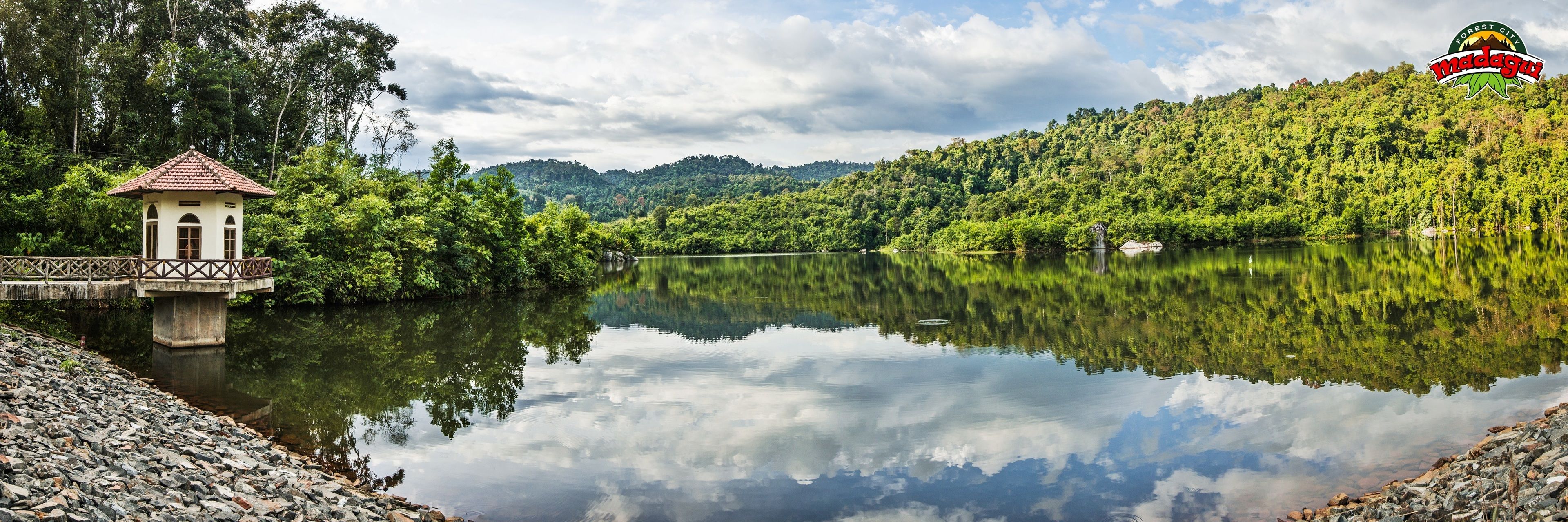 A serene lakeside view with a small white building with a red roof near the water's edge.