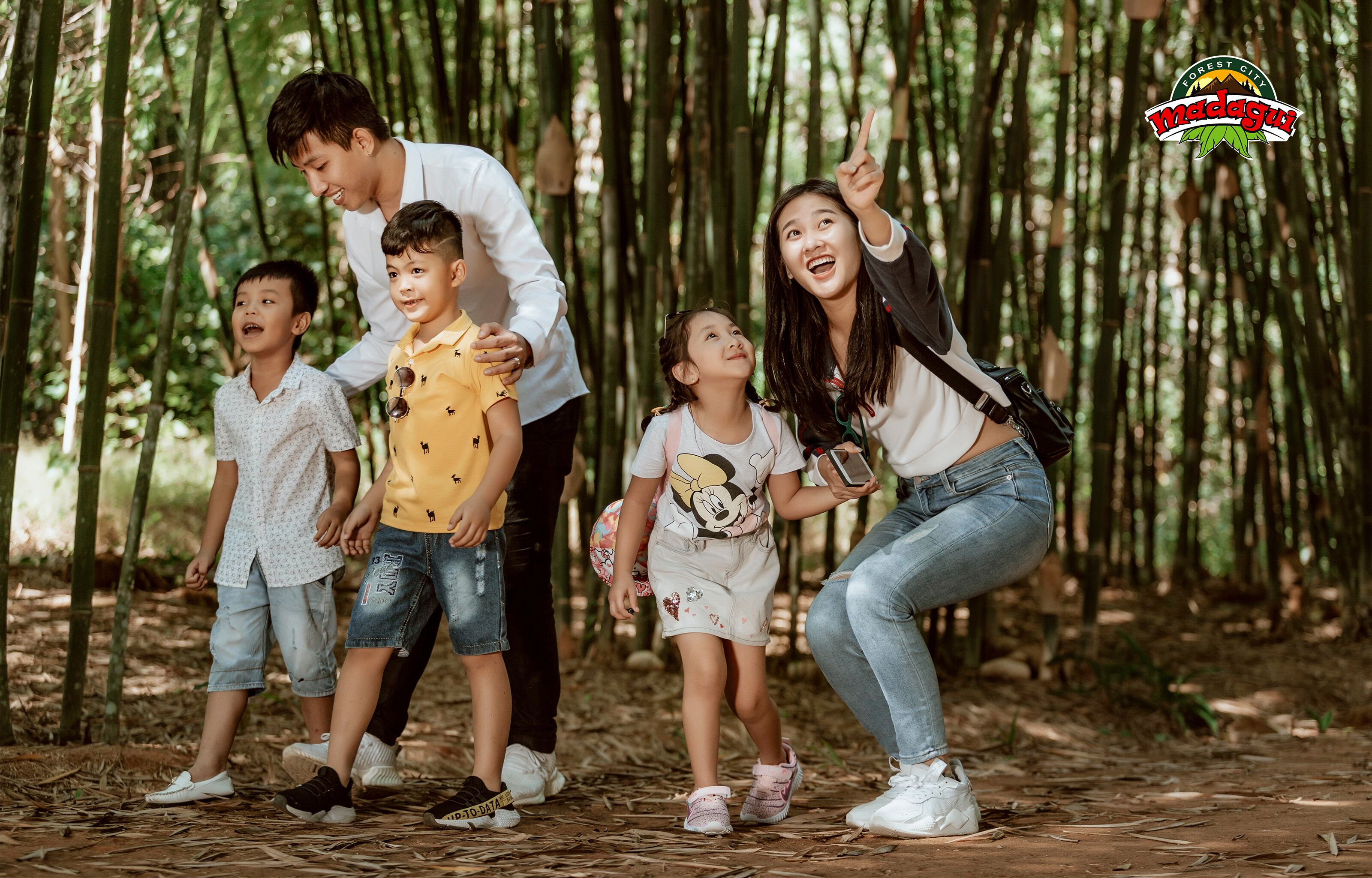 A family in a bamboo forest with a logo in the top right corner.