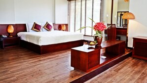 Habitación de hotel con una cama grande, suelo de madera, un escritorio de madera con un florero y un espejo.
