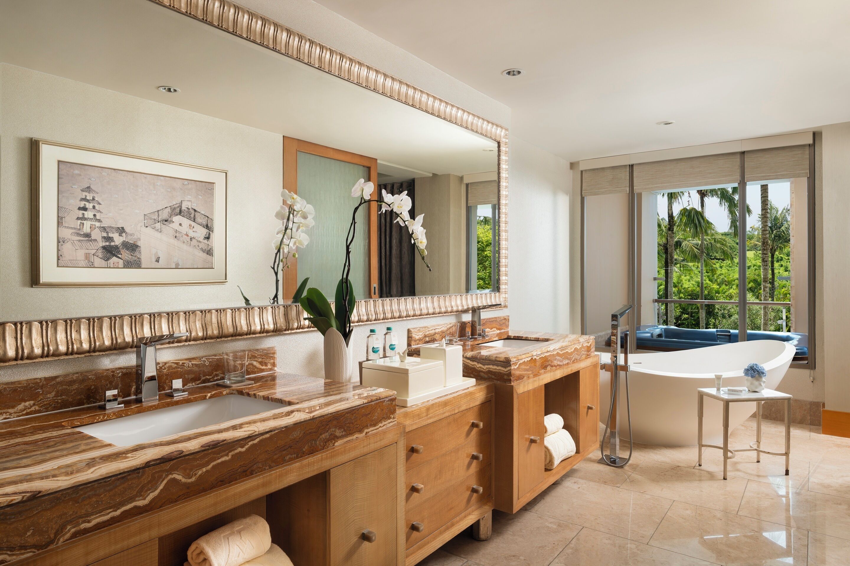 A modern bathroom with a large mirror, two sinks, a bathtub, and a view of greenery outside.