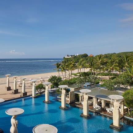 A resort pool with multiple seating areas and a view of the beach.