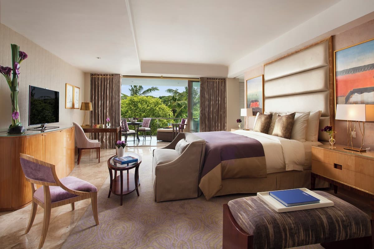 A hotel room with a bed, a desk, a chair, a small table, and a view of the outdoors.