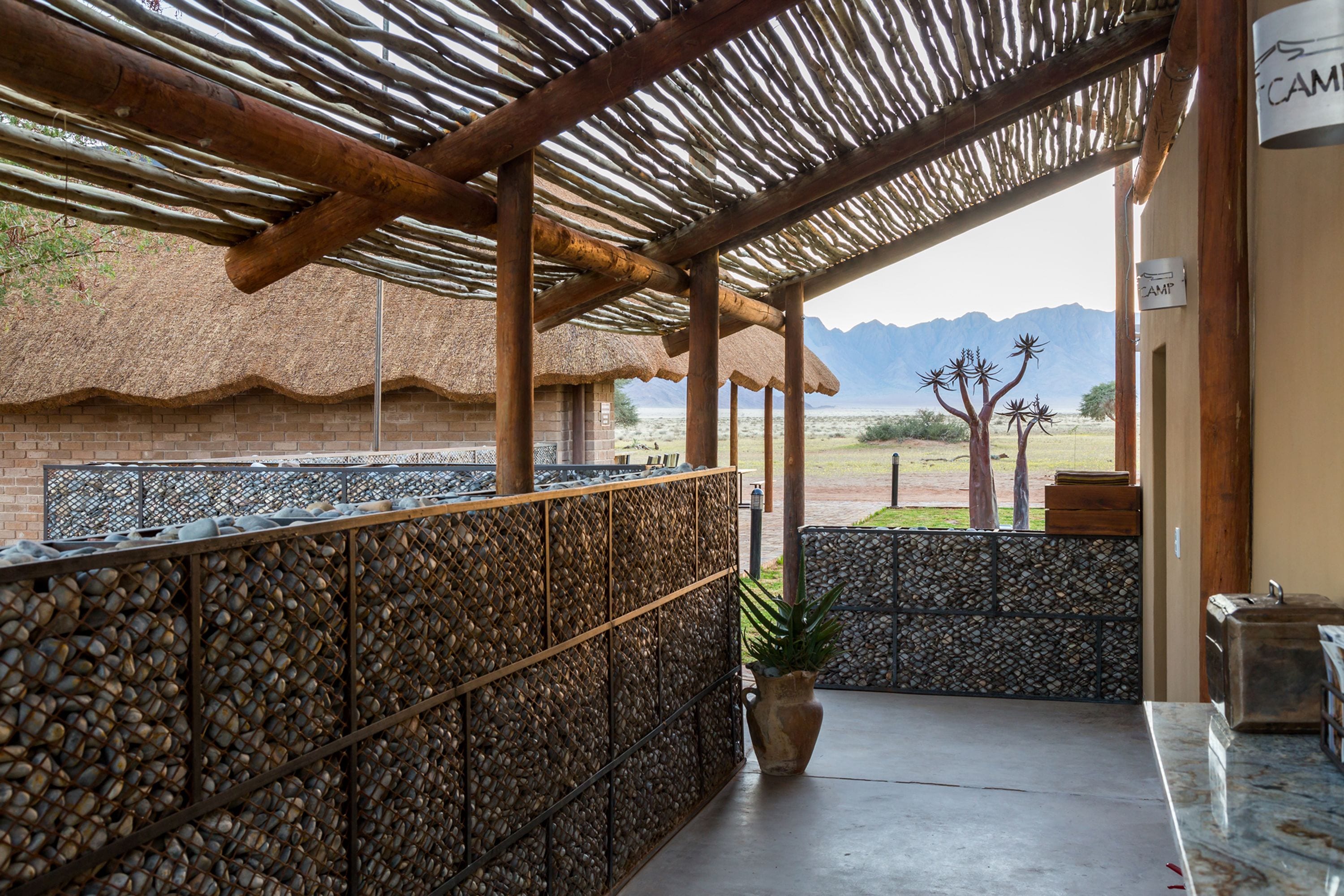 A covered outdoor area with a thatched roof, stone walls, and a view of mountains.