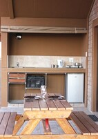 Ein Außenbereich mit einer Küche, einem Holztisch, einem Weinglas und einem Kühlschrank.
