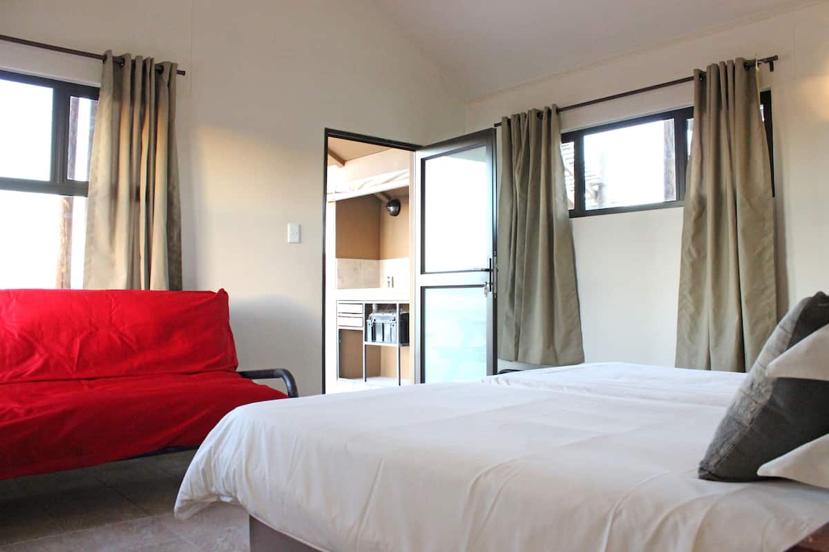 Quarto de hotel com cama, sofá vermelho e janela com cortinas.