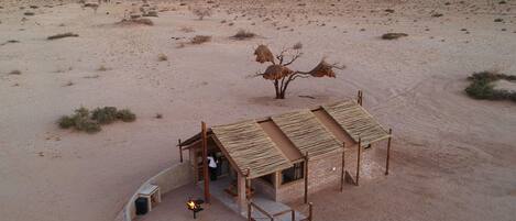 A desert landscape with a small, rustic building featuring a thatched roof and brick walls.
