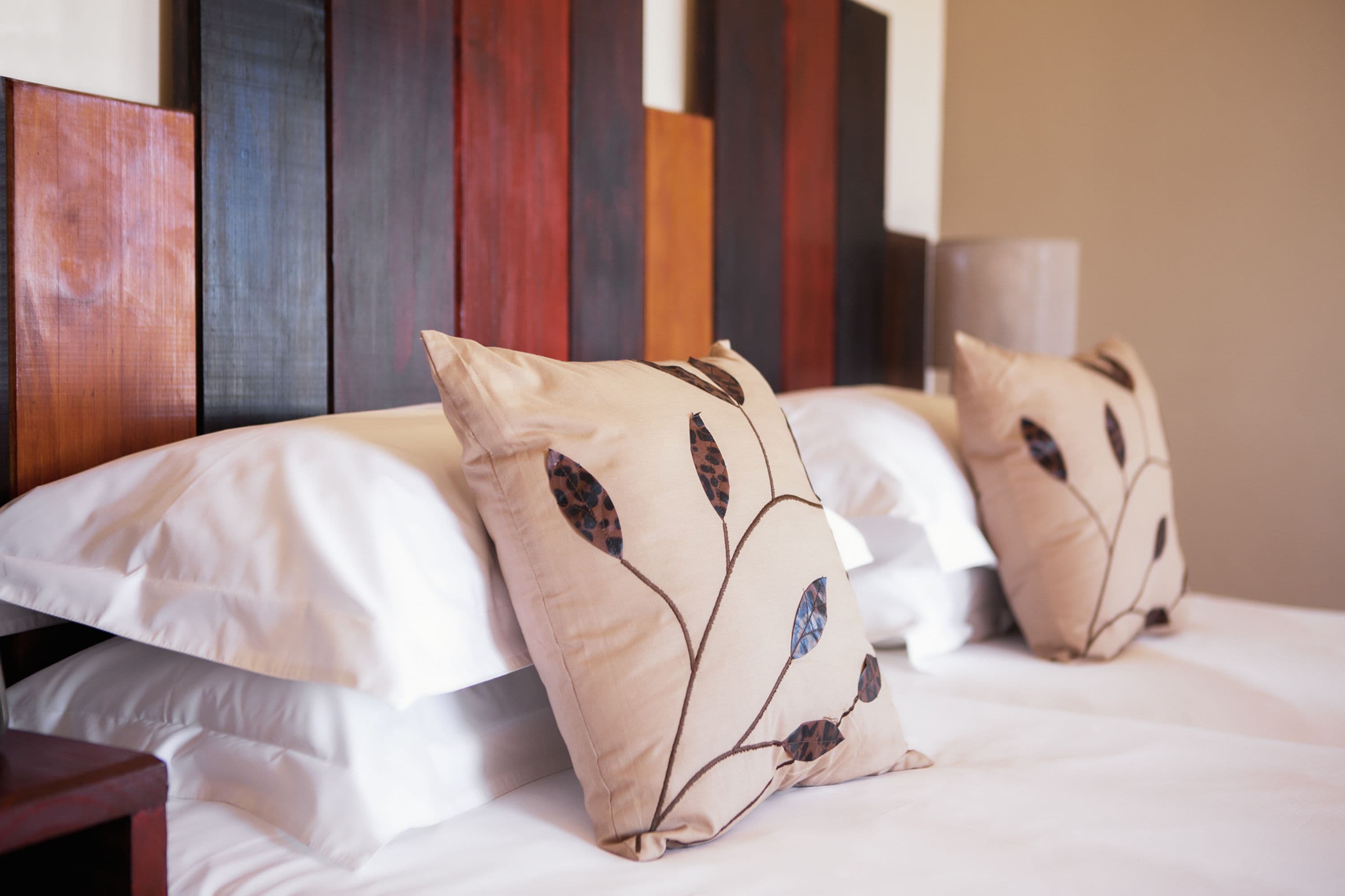 Un lit avec une literie blanche et des coussins décoratifs ornés de motifs de feuilles.