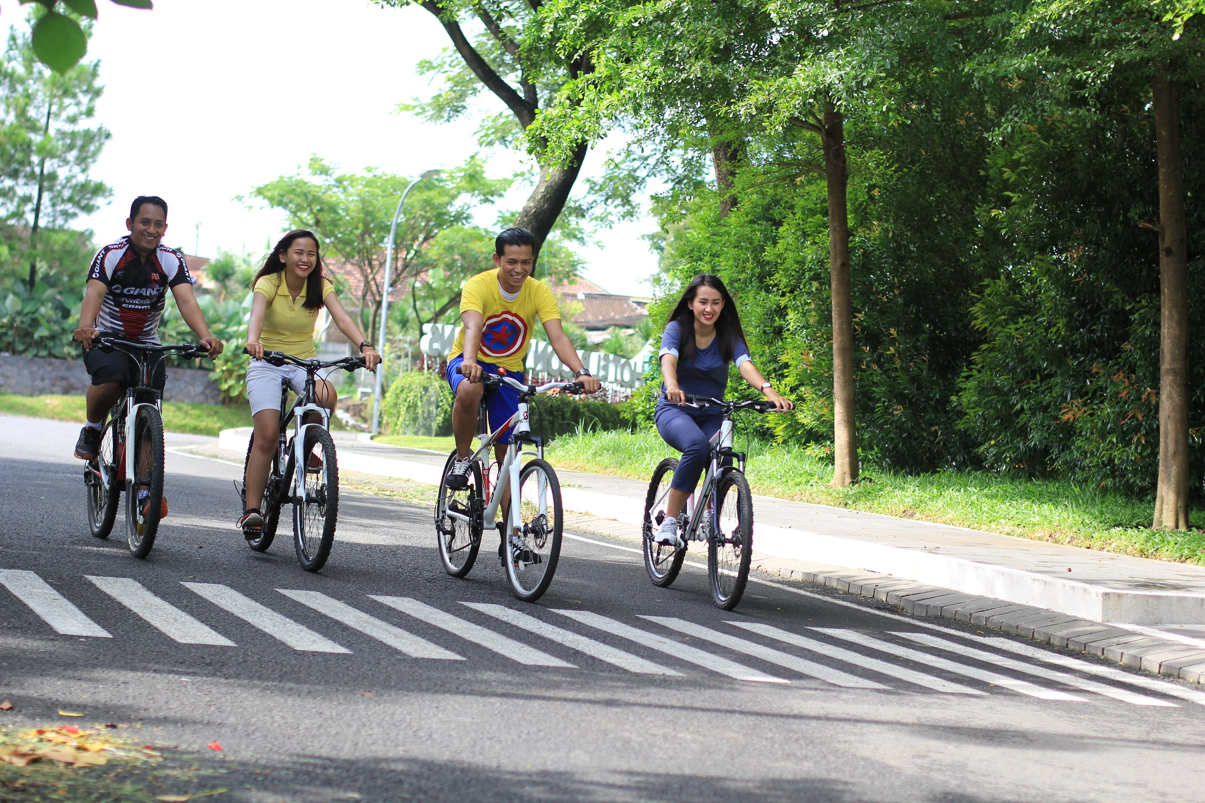 Cuatro personas pedaleando en bicicleta por una carretera con árboles y un paso de peatones.