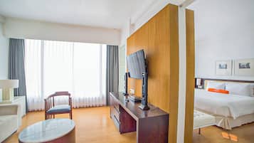 A hotel room with a bed, a desk with a computer, a chair, a TV, and a window with curtains.