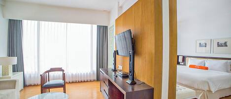 Habitación de hotel con cama, escritorio con computadora, silla, televisor y ventana con cortinas.