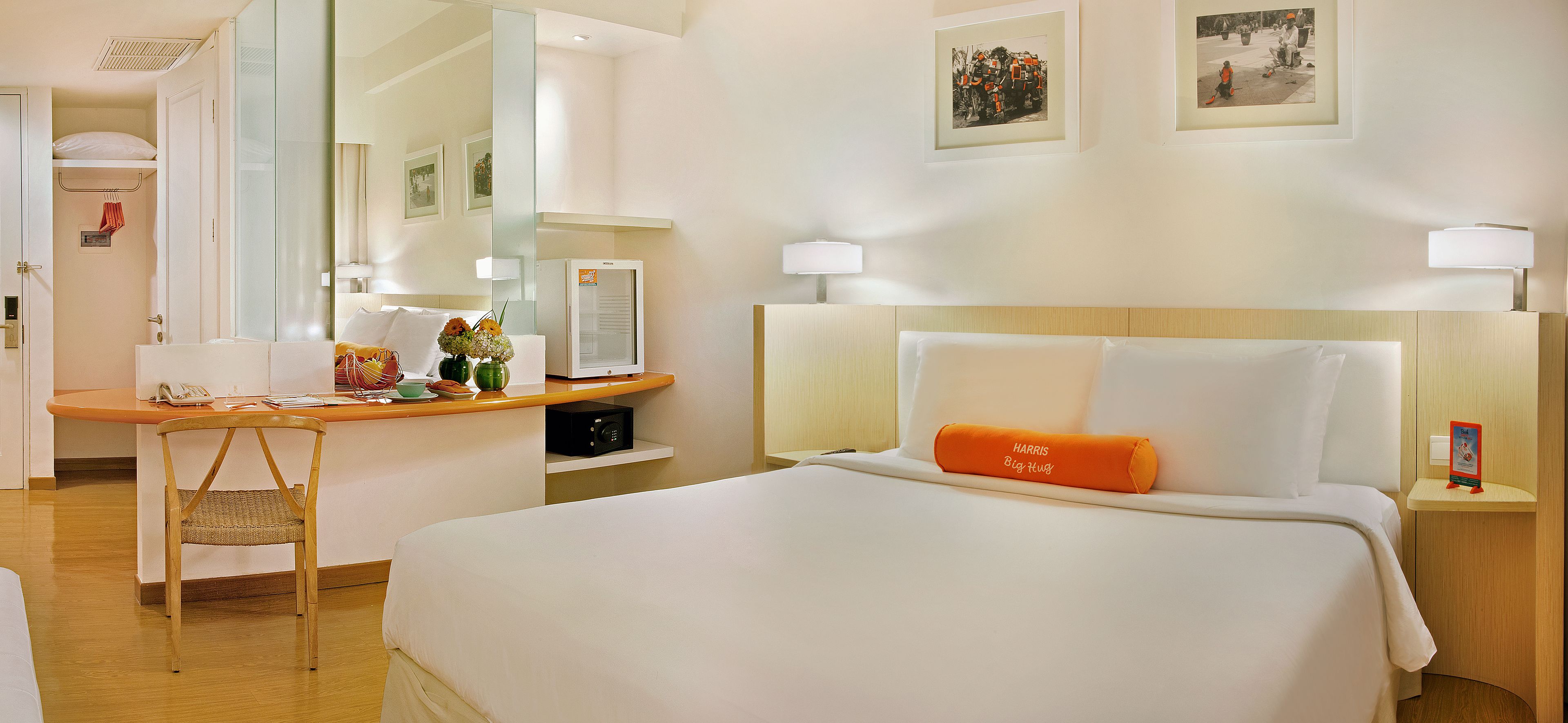 A hotel room with a bed, a desk, a chair, a bedside table, and a mirror.