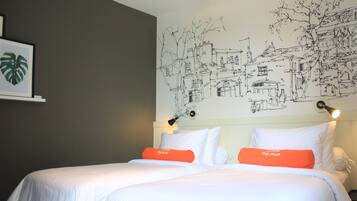Une chambre d’hôtel avec un grand lit, du linge de lit blanc et un oreiller orange. Un mur est décoré d’une fresque représentant une scène de ville.